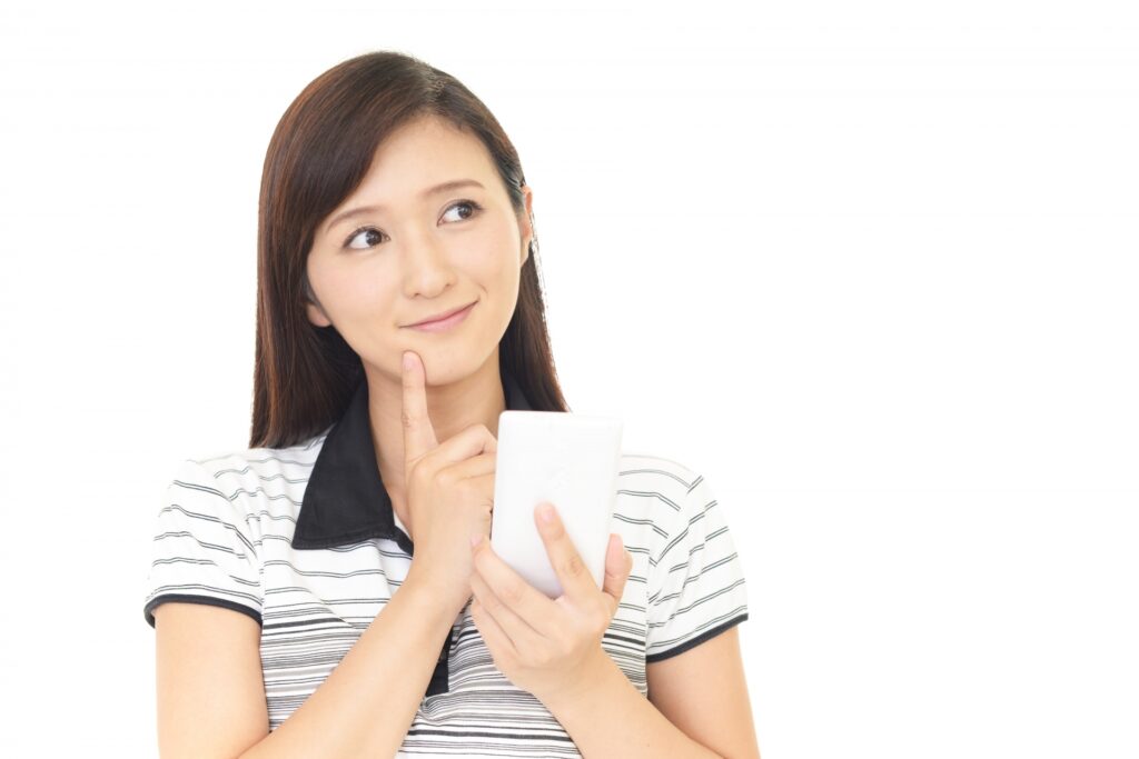 女性がスマホを持ち、考えている写真